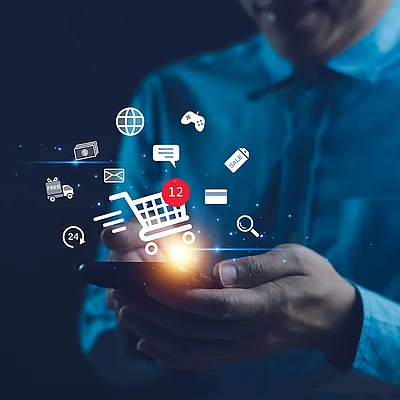 Person nutzt Smartphone für Online-Shopping, mit schwebenden E-Commerce-Symbolen und Warenkorb-Anzeige.