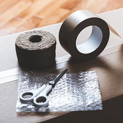 Umzugskarton mit Klebeband, Schere und Verpackungsmaterial als Symbol für Wohnen und Umzug.