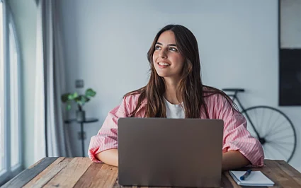 Frau arbeitet am Laptop und blickt optimistisch nach vorn – Symbol für Bildung, Weiterbildung und berufliche Entwicklung.