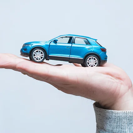 Hand hält Modellauto mit Schutzsymbol als Darstellung von Kfz-Versicherung, Sicherheit und finanzieller Absicherung im Straßenverkehr.