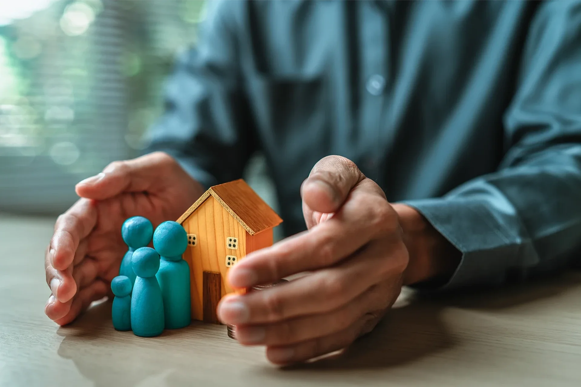 Hände schützen Modellhaus und Familie – Symbol für umfassende Versicherung und finanzielle Absicherung.